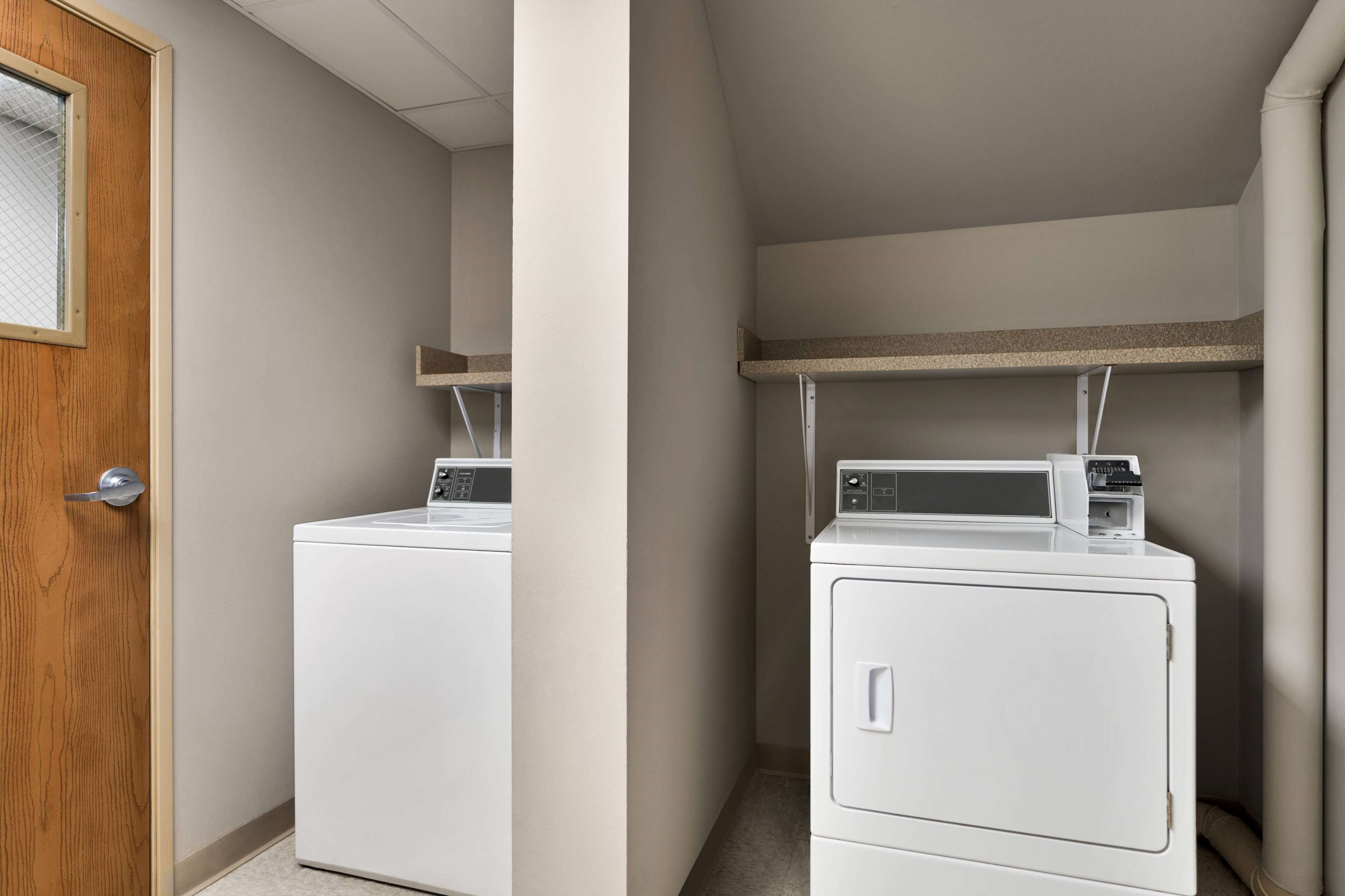 A laundry room with two stacked washers and dryers, a wooden door, and a shelf above the dryers.