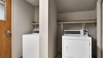 A laundry room with two stacked washers and dryers, a wooden door, and a shelf above the dryers.