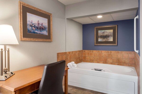 A bathroom with a wooden desk, a chair, a white bathtub, and two framed pictures on the wall.