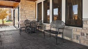 Un patio cubierto con paredes de piedra, ventanas grandes y mobiliario exterior.
