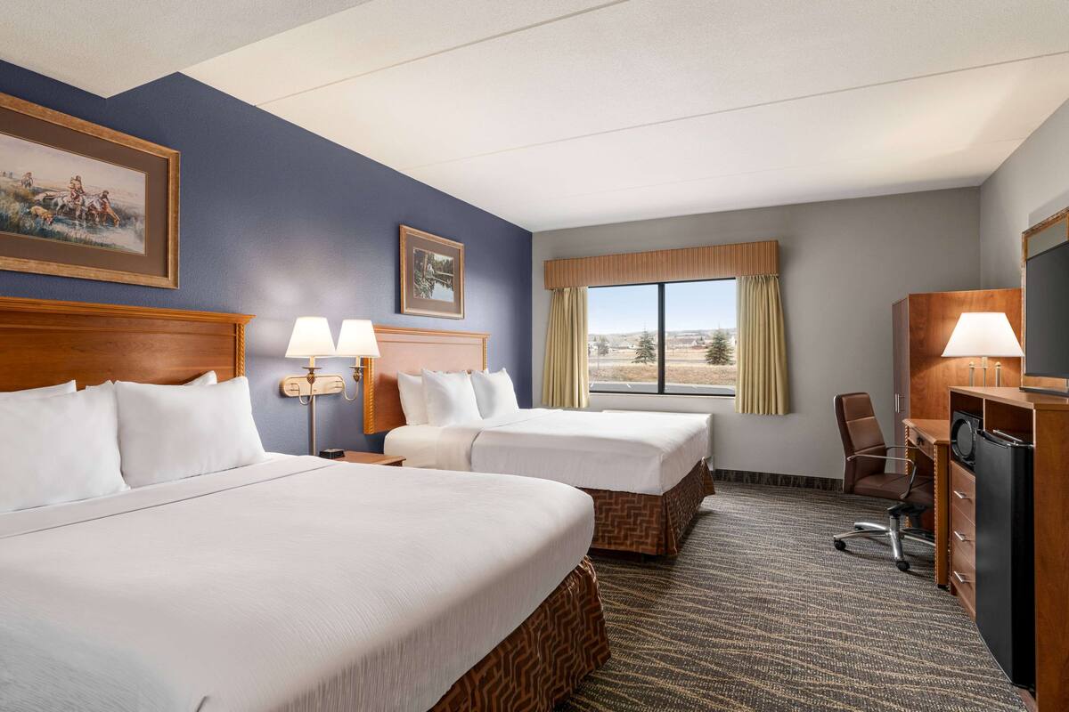 Ein Hotelzimmer mit zwei Betten, einem Schreibtisch, einem Sessel und einem Fernseher.