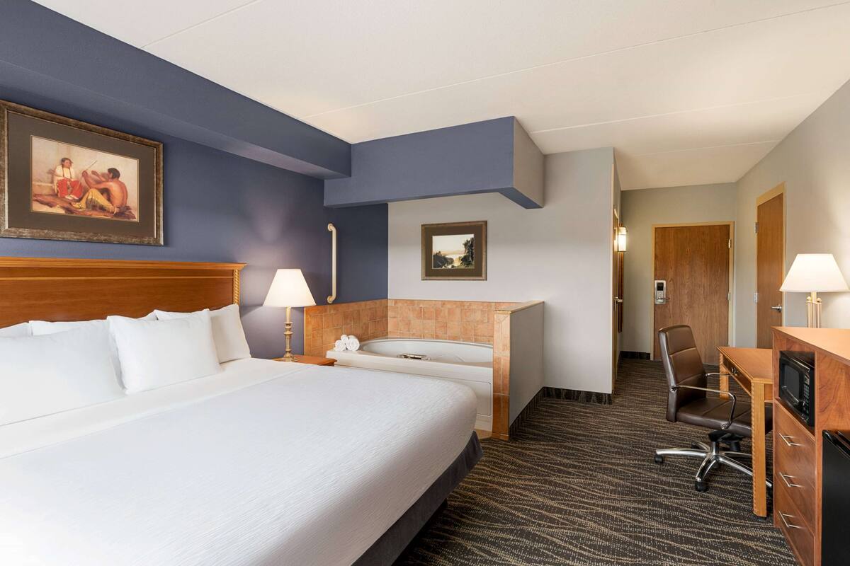Ein Hotelzimmer mit einem großen Bett, einem Schreibtisch, einem Sessel, einer Mikrowelle und einem Badezimmer mit Badewanne.
