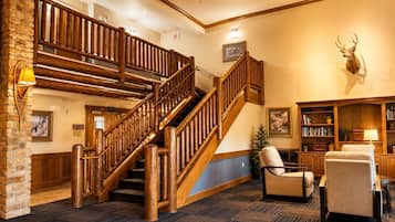 A lobby with a wooden staircase, a fireplace, a bookshelf, and a mounted deer head.