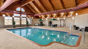 Una piscina interior con techo de madera, paredes de azulejos y una zona de estar con mesas y sillas.