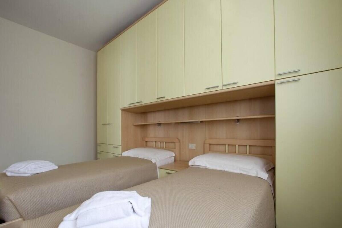 A hotel room with two single beds, a wooden headboard, and a large wardrobe with multiple drawers.