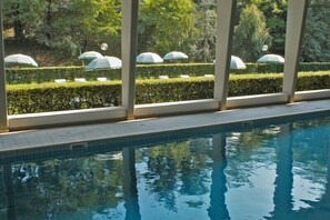 Une piscine à l’eau claire, entourée de haies soigneusement taillées et de parasols.