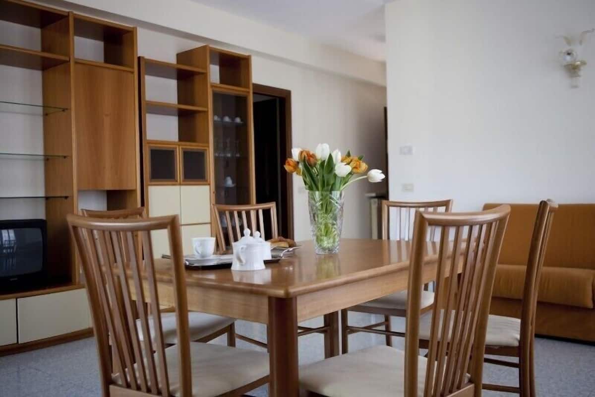 A dining area with a wooden table and chairs, a vase with flowers, and a glass cabinet with shelves.