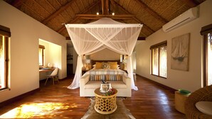 A room with a canopy bed, wooden flooring, a desk with a chair, and a dining table with a placemat. - Azura Benguerra Island (Benguerra Island)