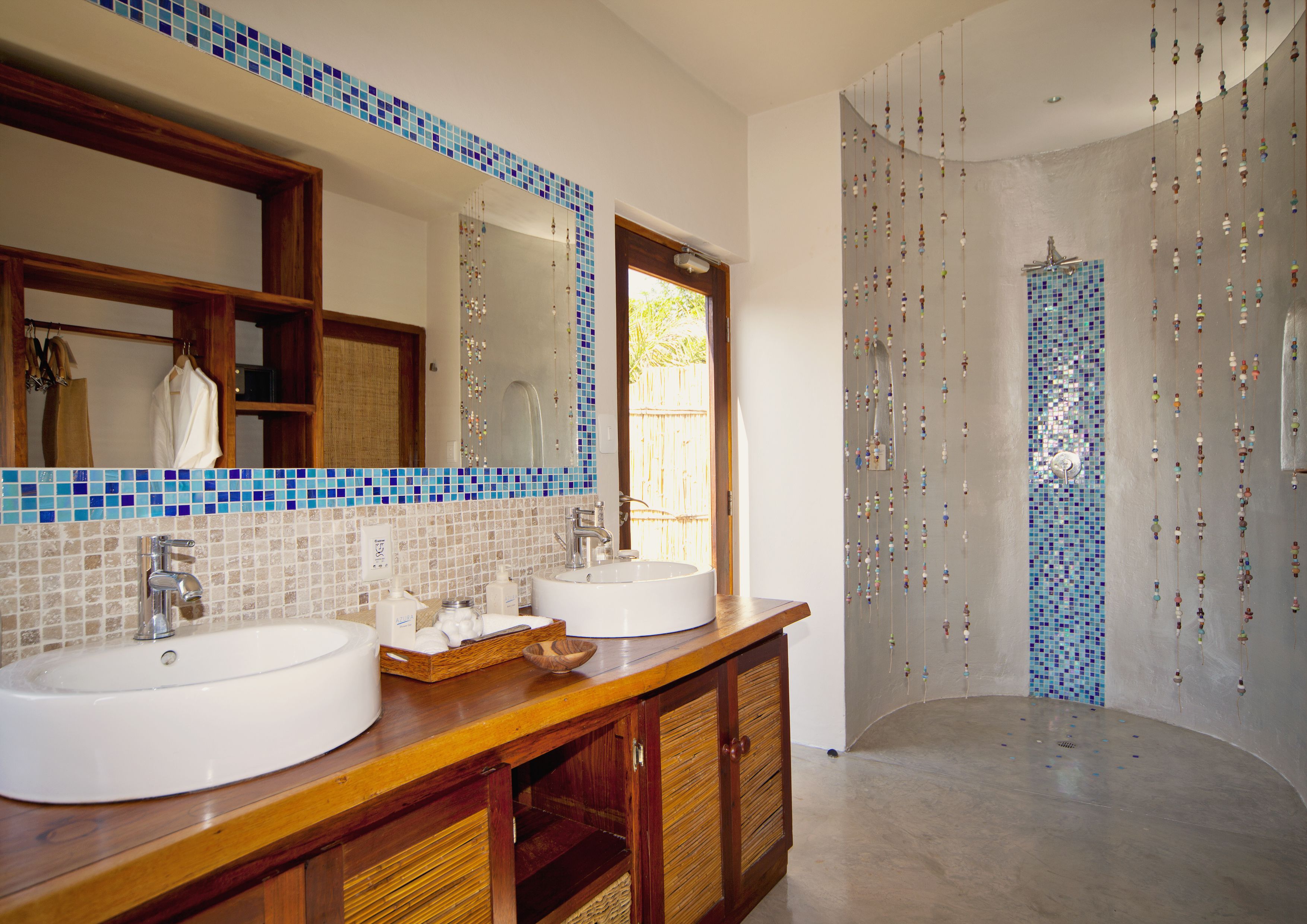 A bathroom with two sinks, a large mirror, and a shower area with blue mosaic tiles.
