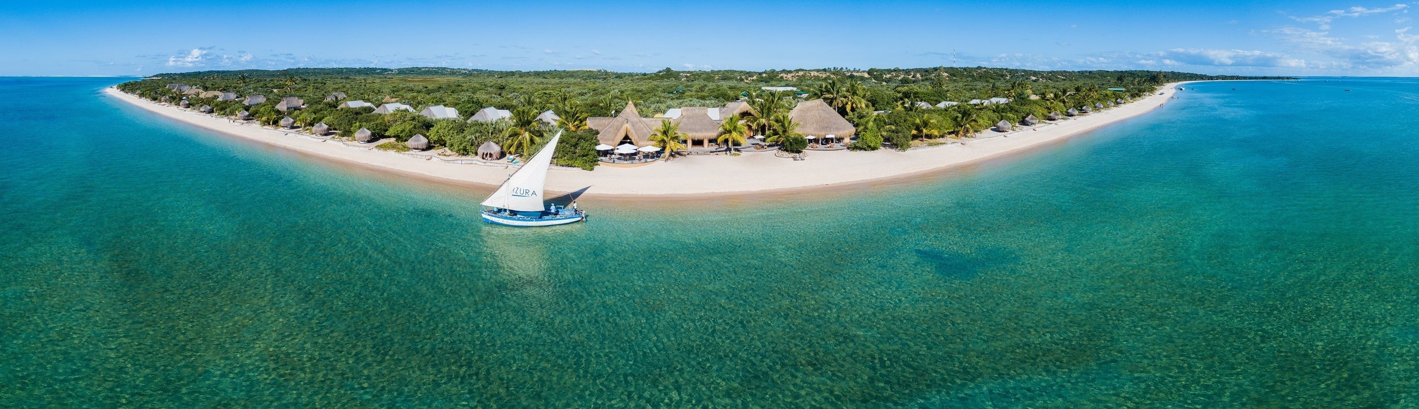 An aerial view of a tropical island with clear turquoise waters, a sandy beach, and thatched-roof structures.