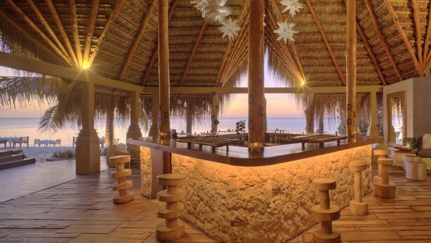 A beachside lounge with a thatched roof, a bar area, and a seating arrangement overlooking the ocean. - Azura Benguerra Island (Benguerra Island)