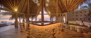 Een strandlounge met rieten dak, een bar en een zithoek met uitzicht op de oceaan.