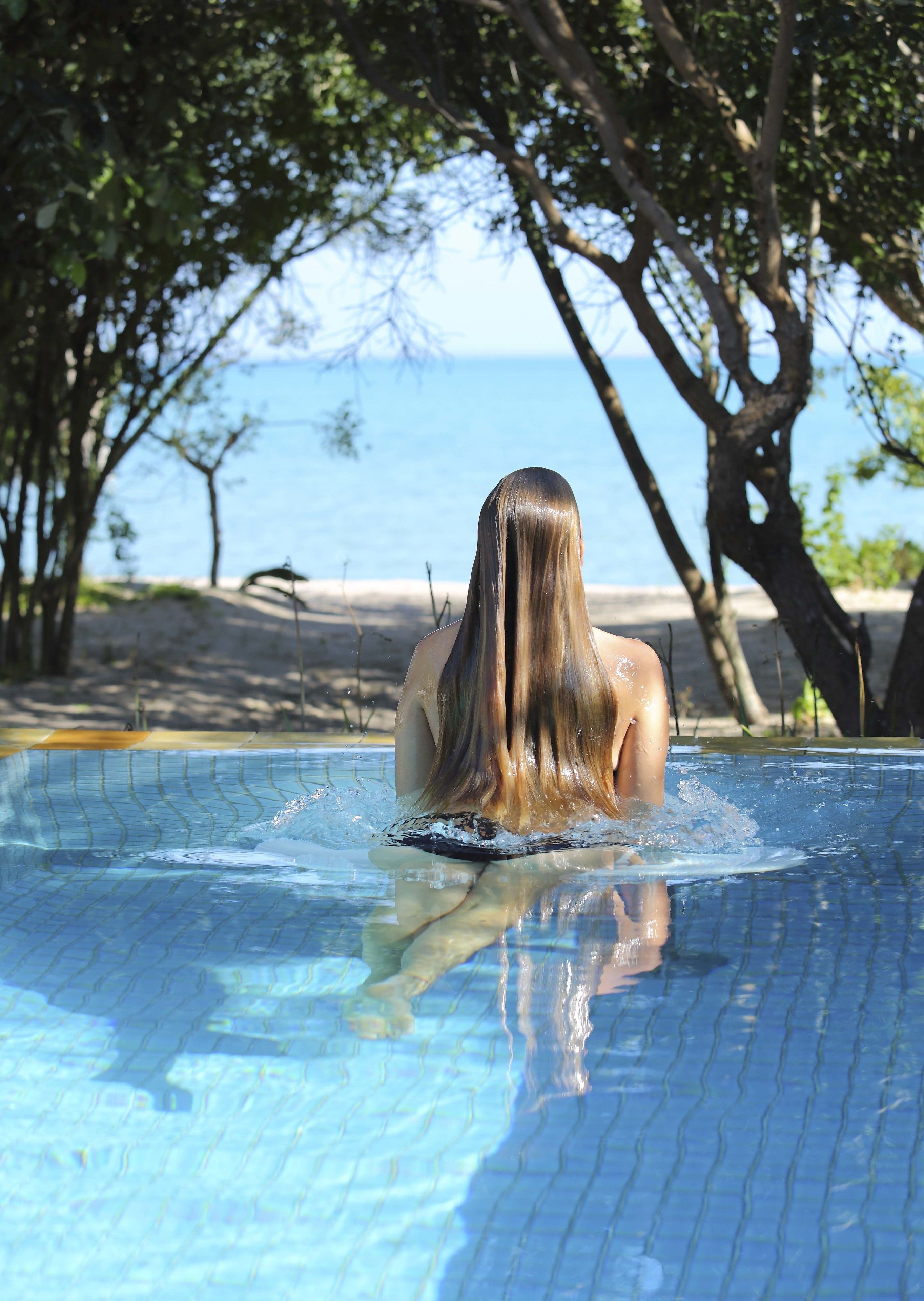 Eine Person in einem Schwimmbecken mit Blick auf das Meer und Bäume im Hintergrund.