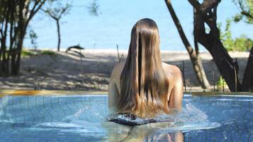 Eine Person in einem Schwimmbecken mit Blick auf das Meer und Bäume im Hintergrund.