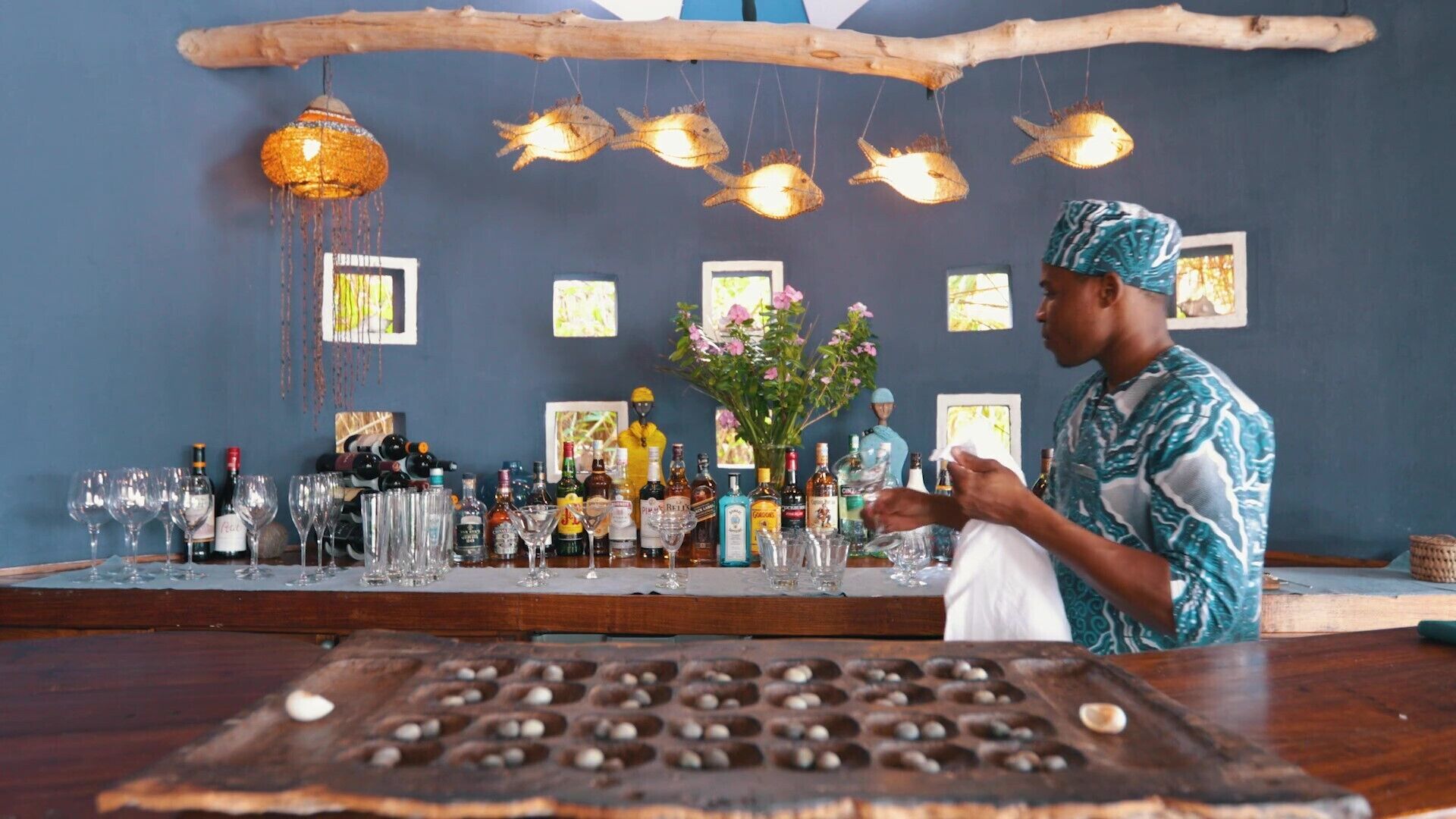 A bar with a variety of bottles and glasses, a decorative hanging light, and a wooden tray with round objects.