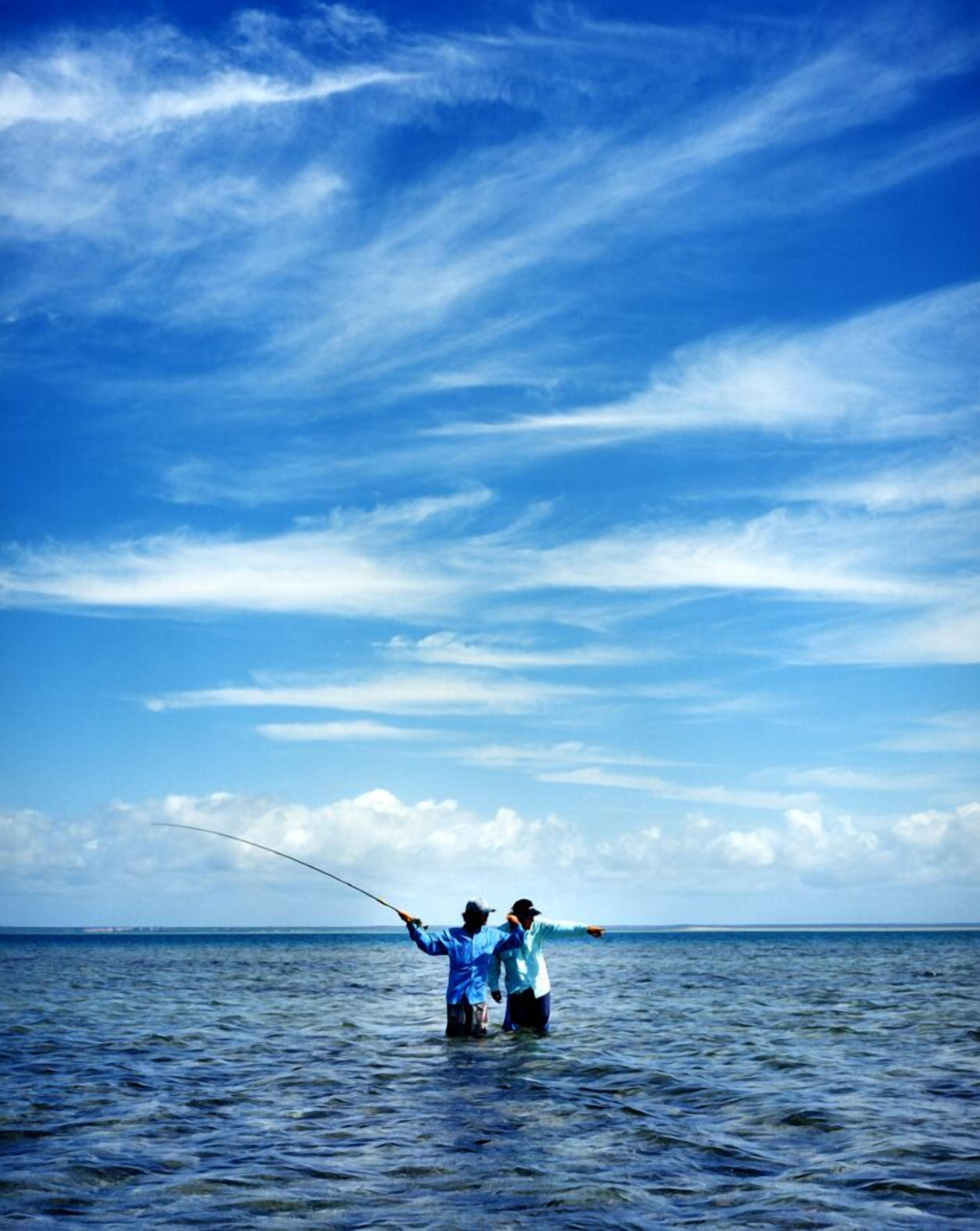 Two people fishing in a body of water under a clear blue sky.