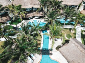 An aerial view of a resort with a central swimming pool, palm trees, and thatched-roof structures. - El Dorado Casitas Royale, All & More Inclusive - Adults Only (Playa del Carmen)