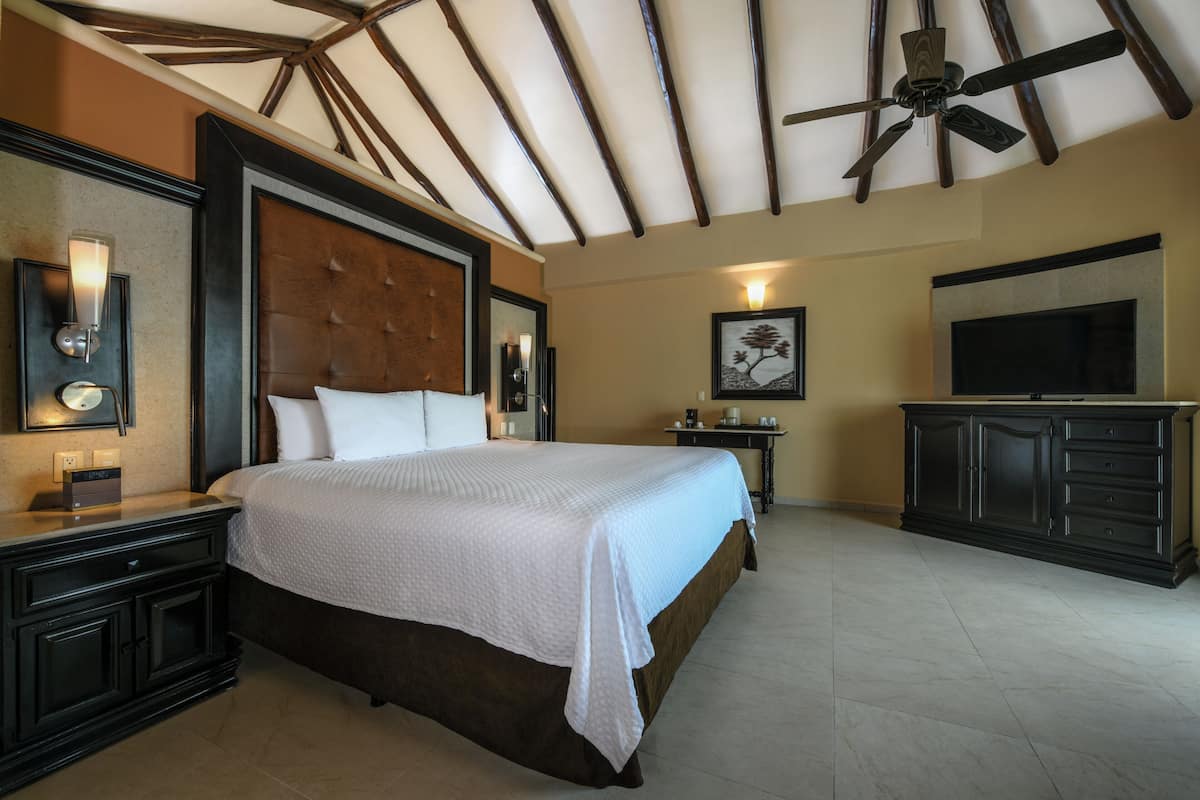 A hotel room with a large bed, a ceiling fan, a television, and a desk with a chair.
