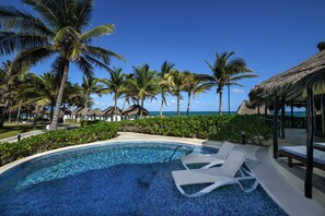 A pool with lounge chairs, palm trees, and a view of the ocean.