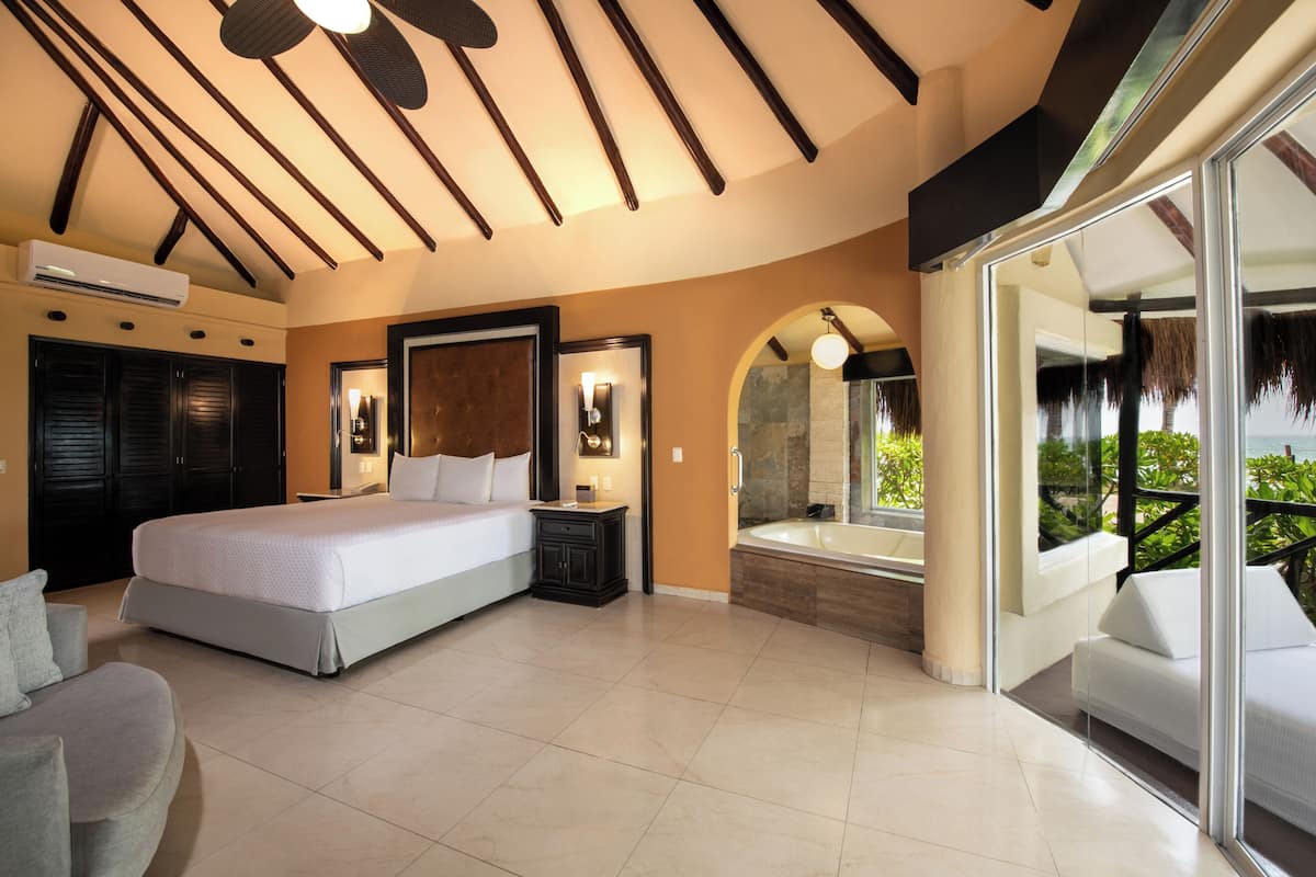 A modern bedroom with a large bed, a built-in bathtub, and a balcony with a view of greenery.