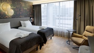 A hotel room with two beds, a round table, a chair, and a large window with curtains.