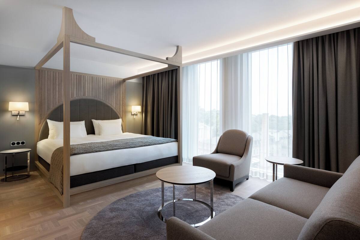 Une chambre d’hôtel moderne dotée d’un lit à baldaquin, d’un canapé, d’une table basse et offrant une vue sur la ville.