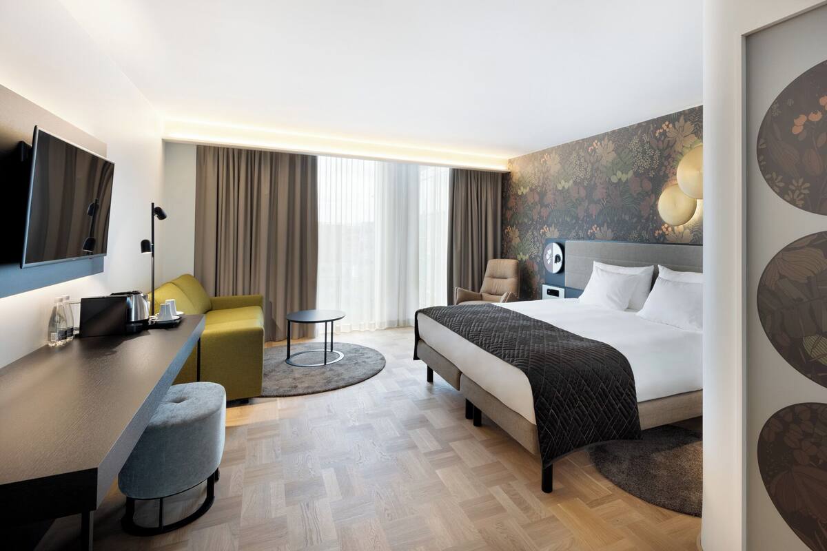 Une chambre d’hôtel moderne équipée d’un lit, d’un bureau, d’une chaise, d’une table ronde et d’un téléviseur.