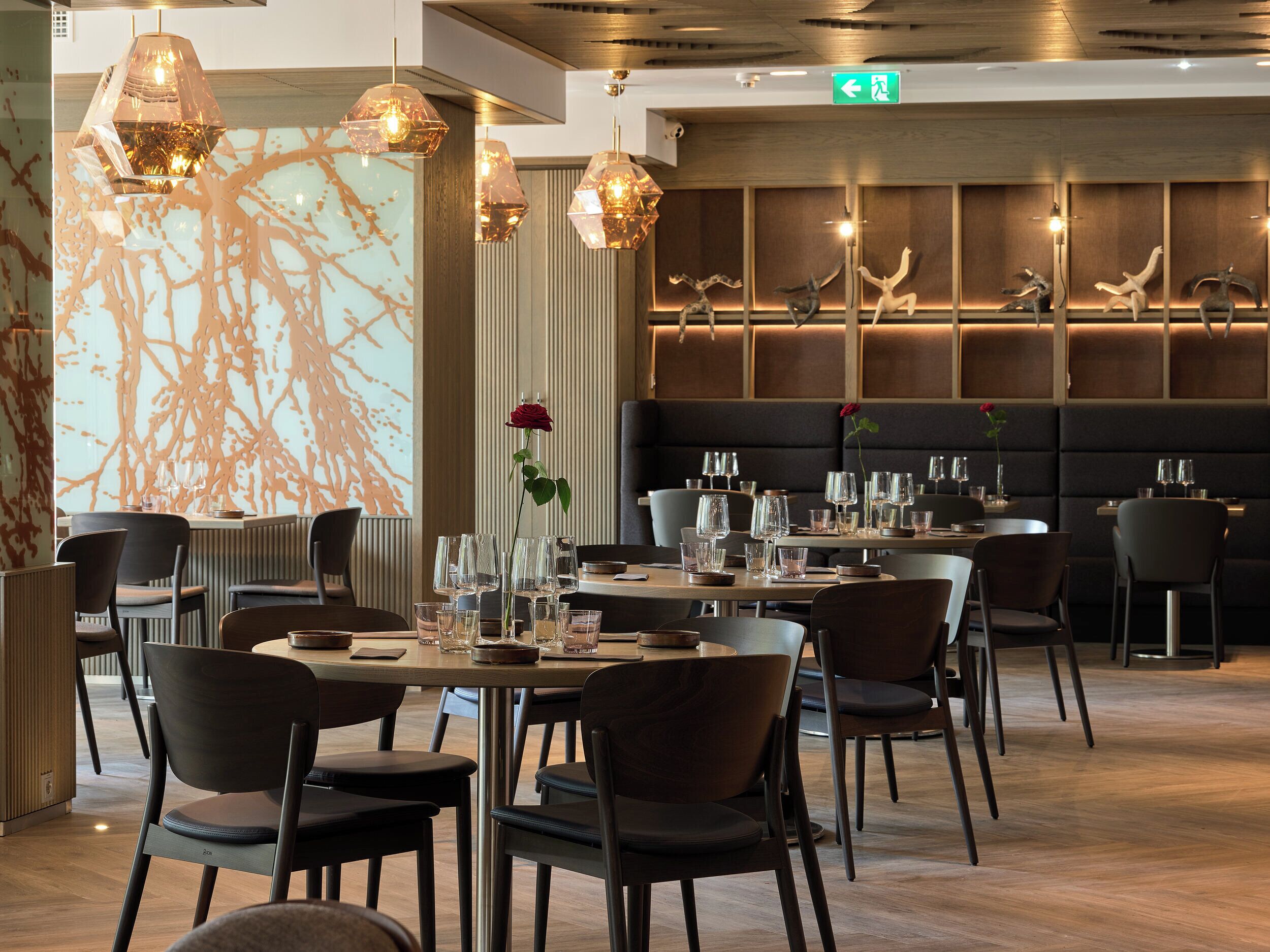 A modern restaurant interior with tables set for dining, pendant lighting, and decorative wall art.