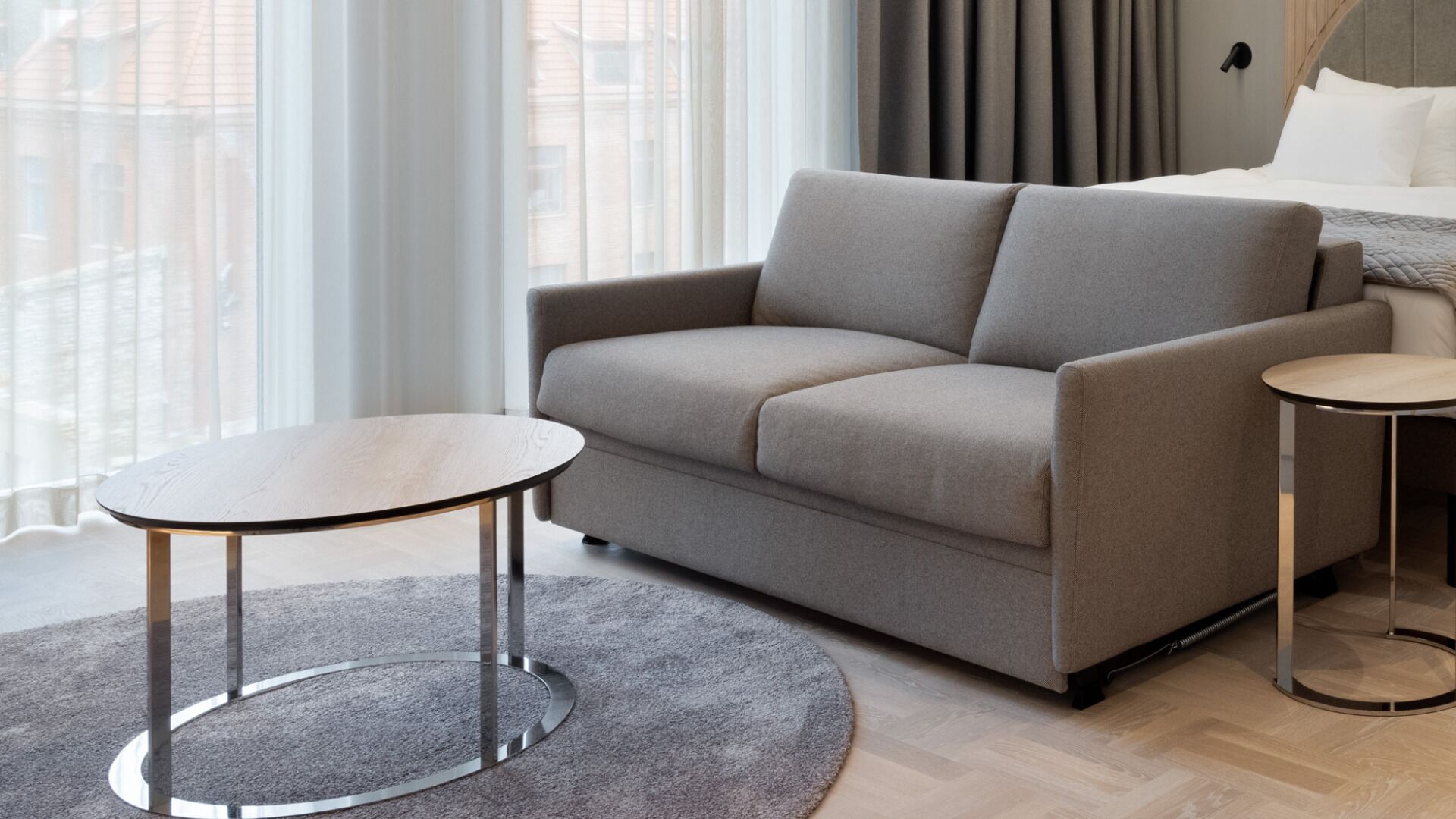Una sala de estar moderna con un sofá gris, dos mesas redondas y una alfombra gris.