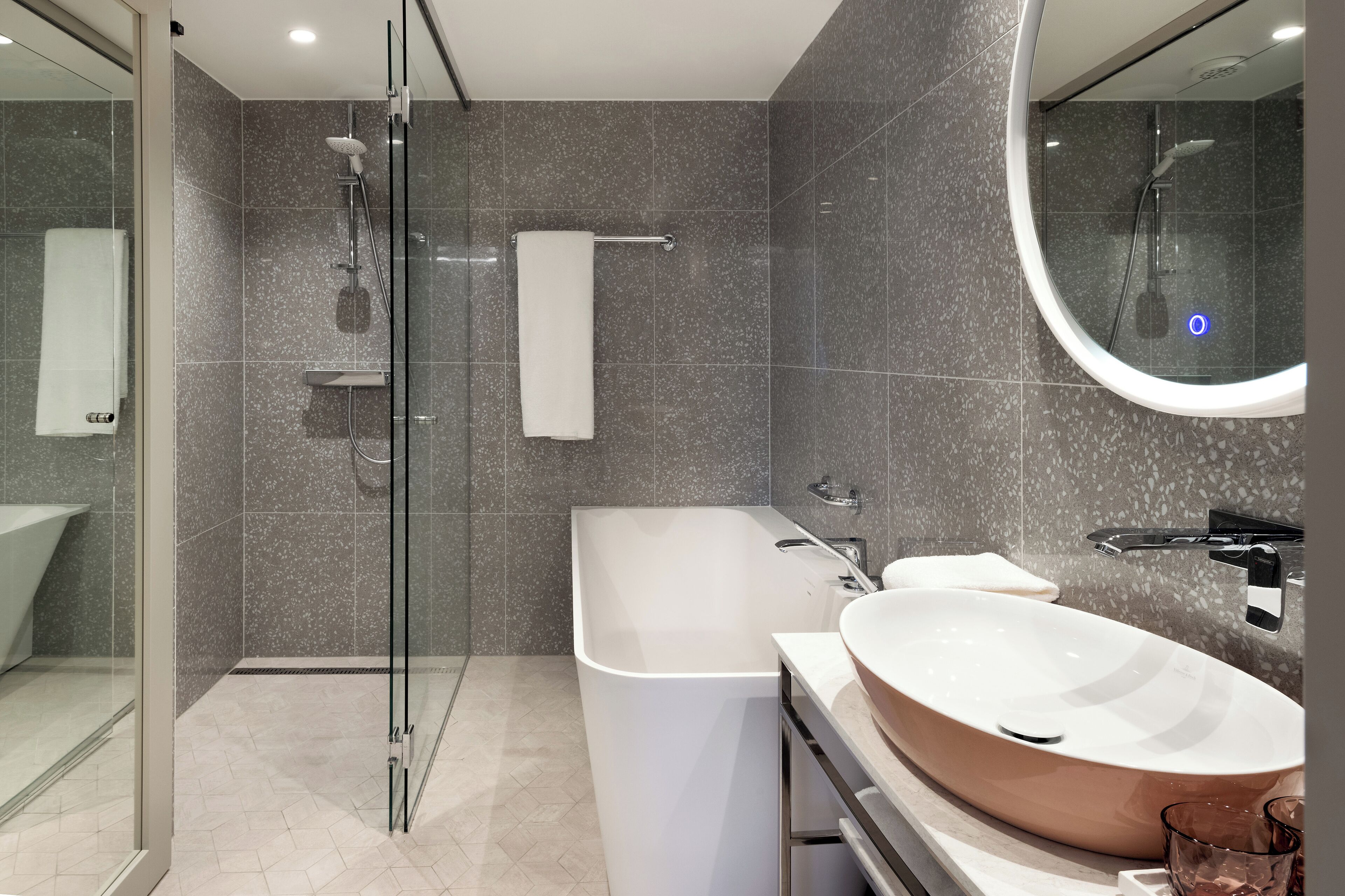 Un baño moderno con ducha envuelta en vidrio, una bañera independiente y un lavamanos ovalado grande.