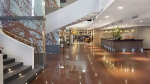 Un moderno vestíbulo de hotel con una escalera central, un mostrador de recepción y un área de descanso.