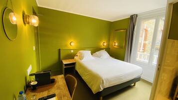 A hotel room with a bed, bedside tables, a desk with a laptop, a mirror, and a window with curtains.