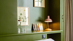 Una habitación con una cama, un escritorio con lámpara, cuadros enmarcados y una estantería llena de libros.