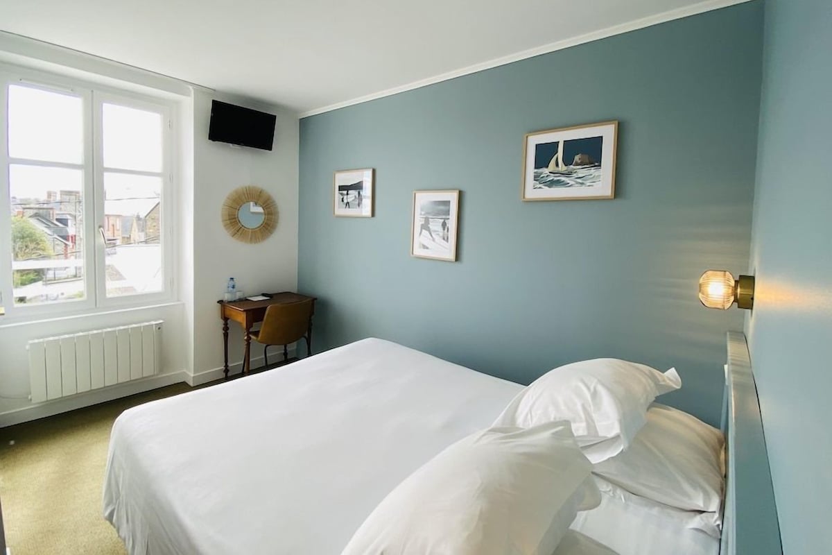 Habitación de hotel con cama, escritorio y ventana con vista a edificios.