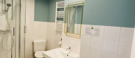 Une salle de bain avec une douche à parois de verre, des toilettes blanches, un lavabo avec un miroir et un porte-serviettes.