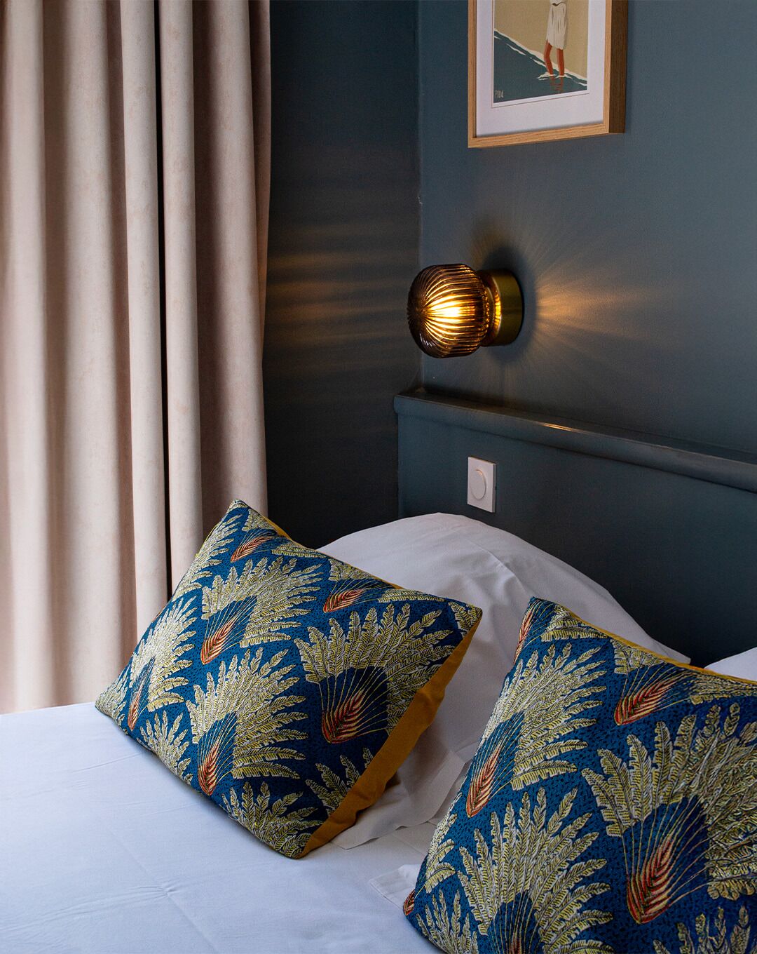A bed with two decorative pillows, a wall-mounted light, and a framed picture on the wall.