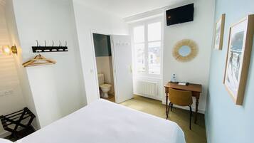 Hotellihuone, jossa on sänky, työpöytä, televisio, ikkuna ja kylpyhuone, joka näkyy avoimesta ovesta.
