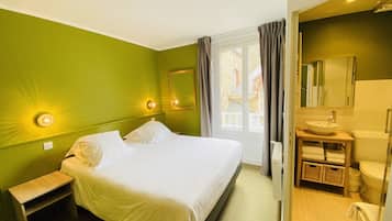 Een hotelkamer met een bed, nachtkastje en een badkamer met een wastafel en spiegel.