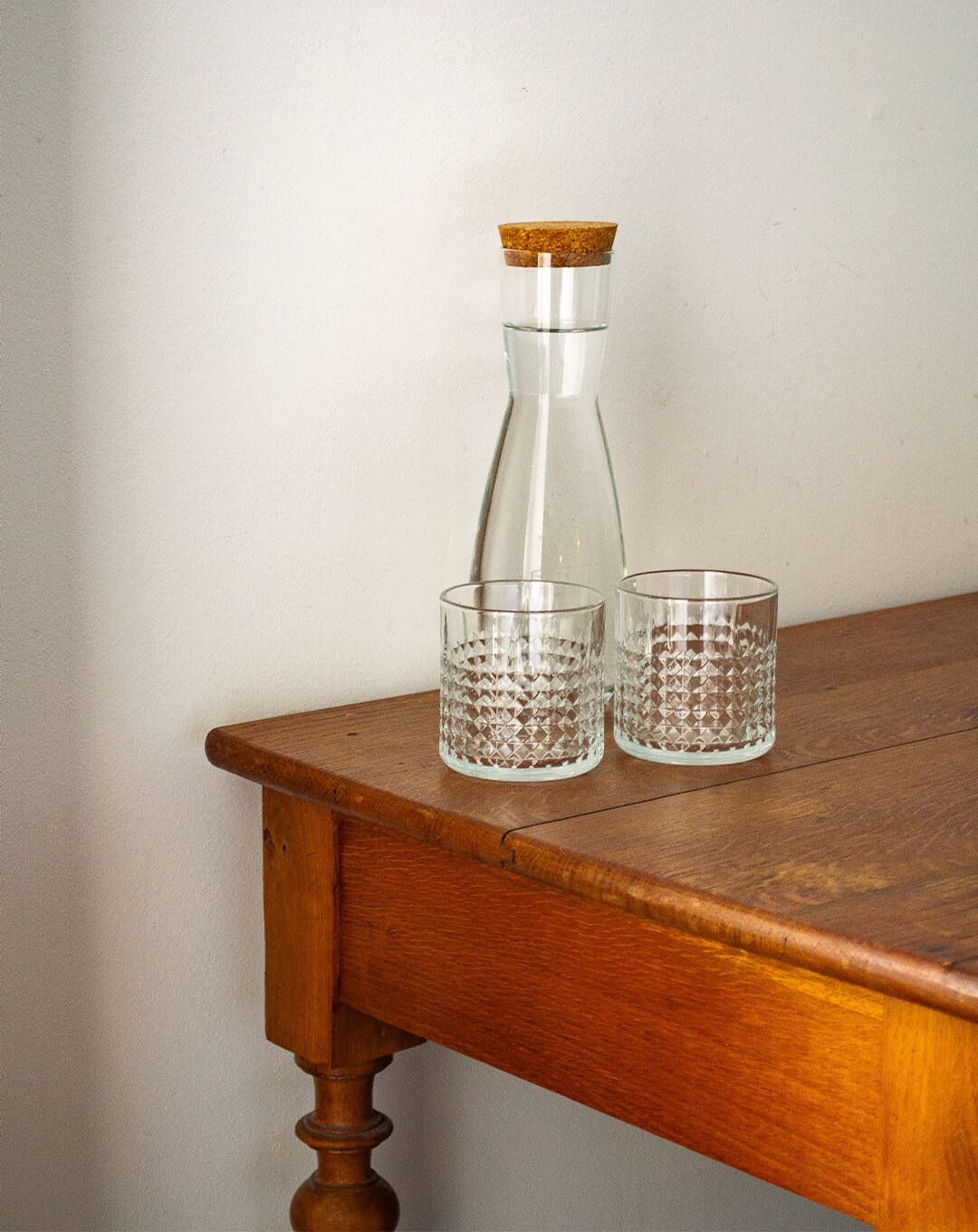 Una mesa de madera con una botella de vidrio transparente y dos vasos de vidrio.