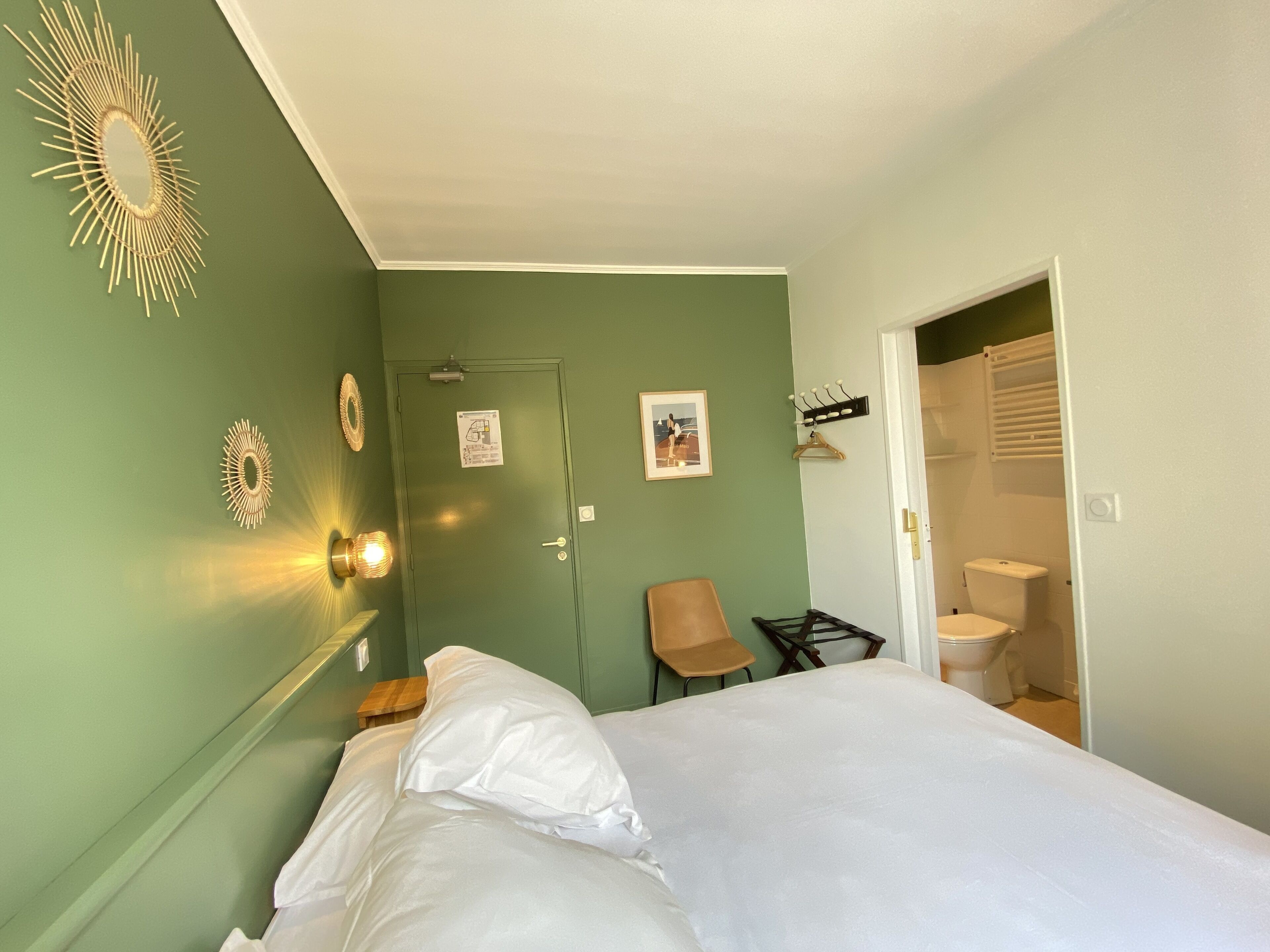 Une chambre à coucher comprenant un lit, une chaise, un porte-manteau et une porte donnant sur une salle de bain.