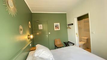 Une chambre à coucher comprenant un lit, une chaise, un porte-manteau et une porte donnant sur une salle de bain.
