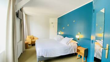 Ein Hotelzimmer mit einem Bett, einem kleinen Holfnachtkästchen, einem Sessel und einer blauen Akzentwand mit Wandleuchten.