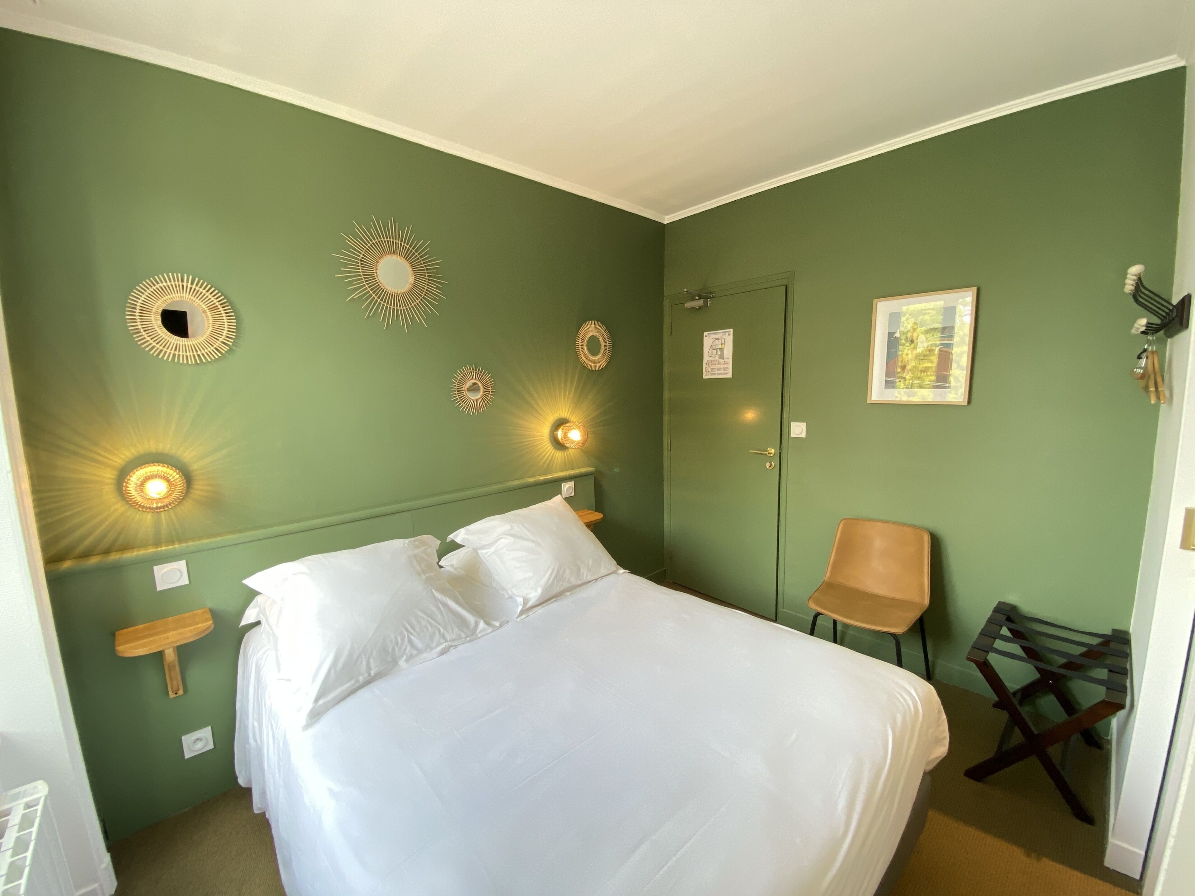 Un dormitorio con cama, apliques de pared, una puerta, una silla y una mesita.