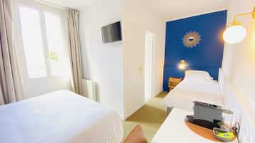 Ett hotellrum med två sängar, ett skrivbord med en bärbar dator, en kaffemaskin och en tv på väggen.