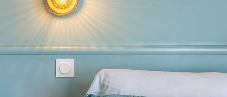 A bedroom with a bed, a wall-mounted light, and a small wooden nightstand.