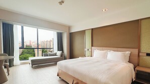 Une chambre d’hôtel moderne dotée d’un grand lit, d’un coin salon près de la fenêtre et offrant une vue sur le paysage urbain.