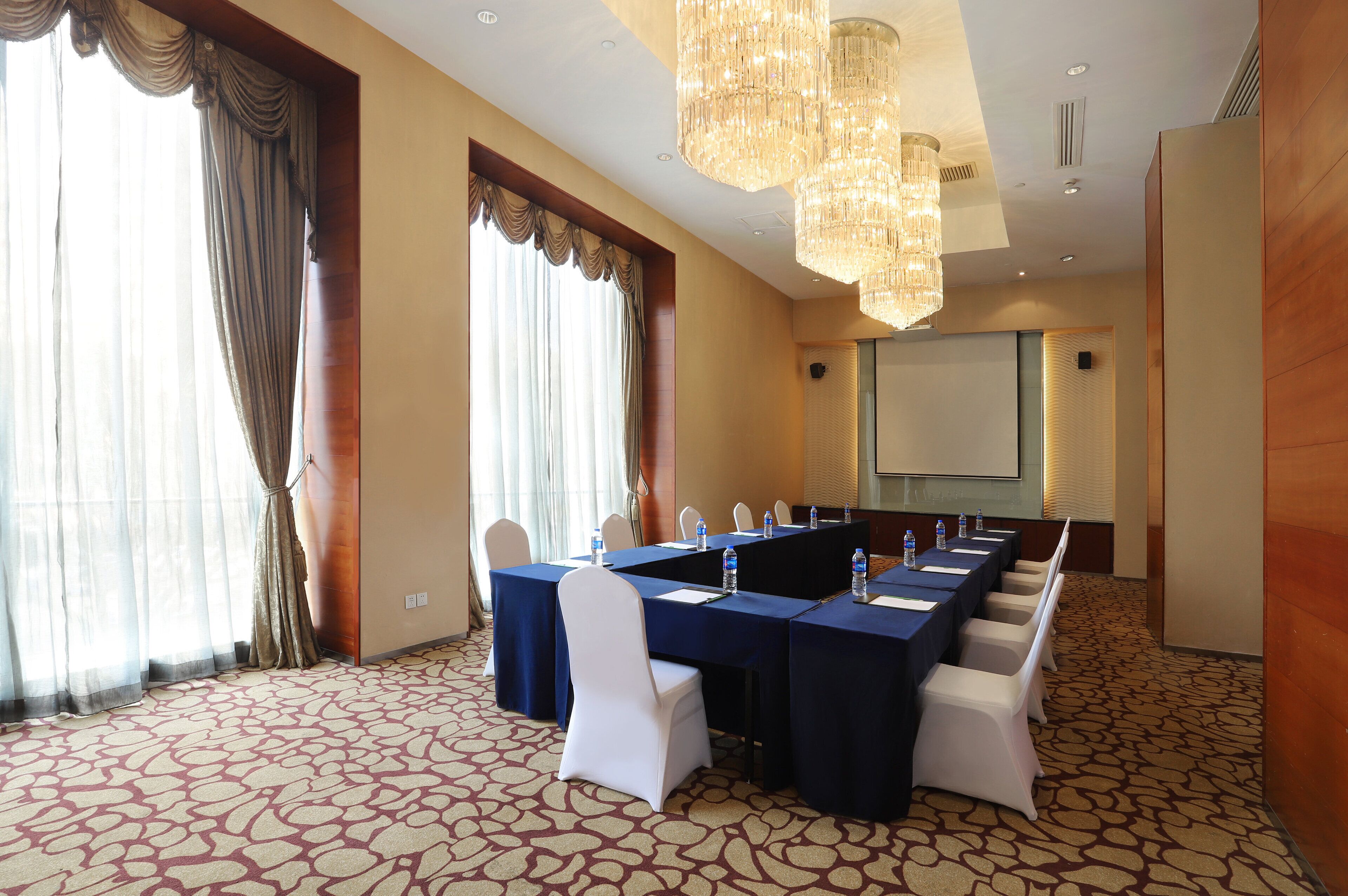 A conference room with a long table, white chairs, and a projector screen.
