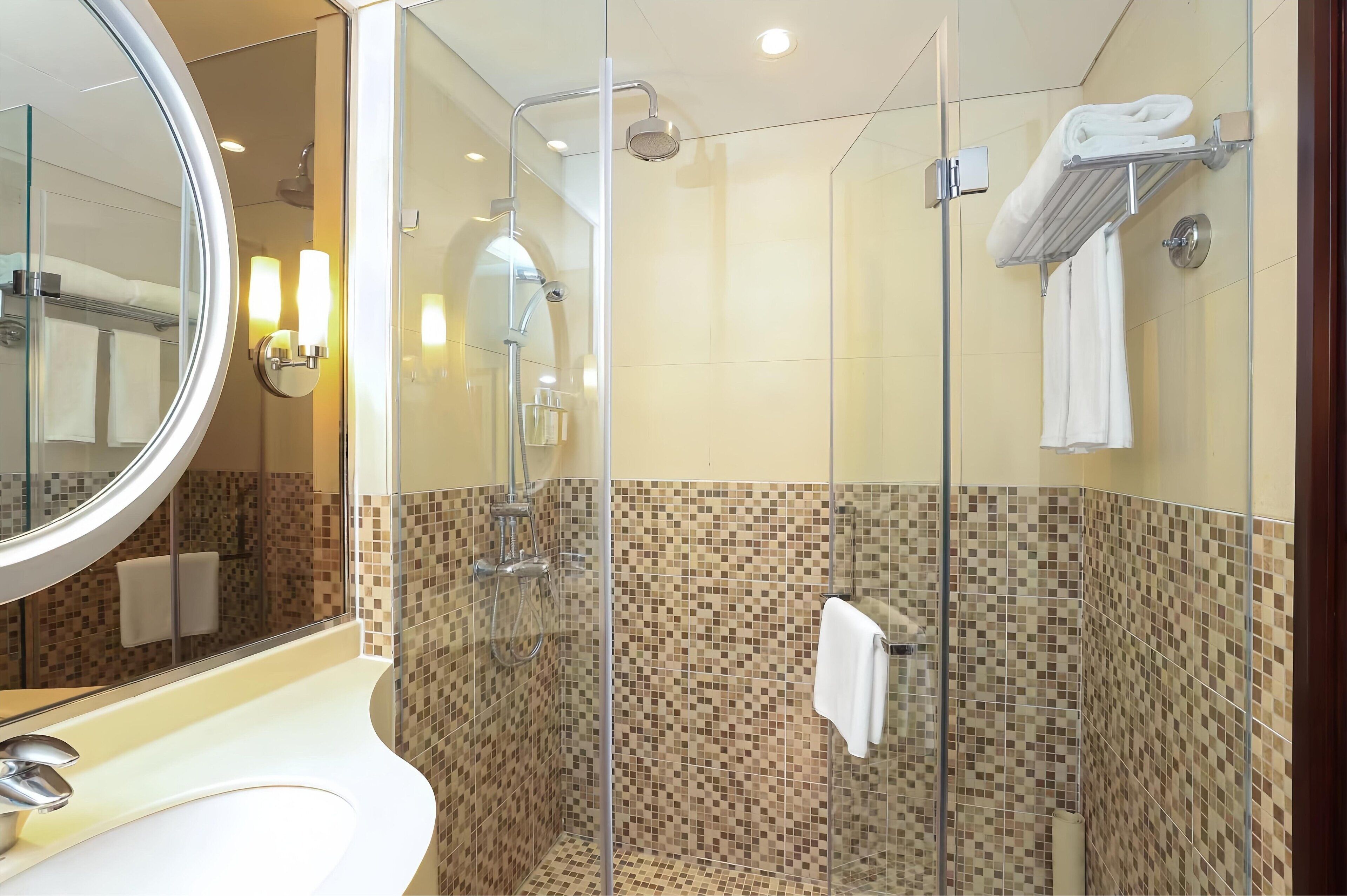 Un baño moderno con cabina de ducha de vidrio, un lavabo blanco y un salpicadero de azulejos.