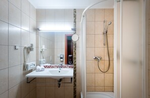 A bathroom with a sink, mirror, towel dispenser, and shower.