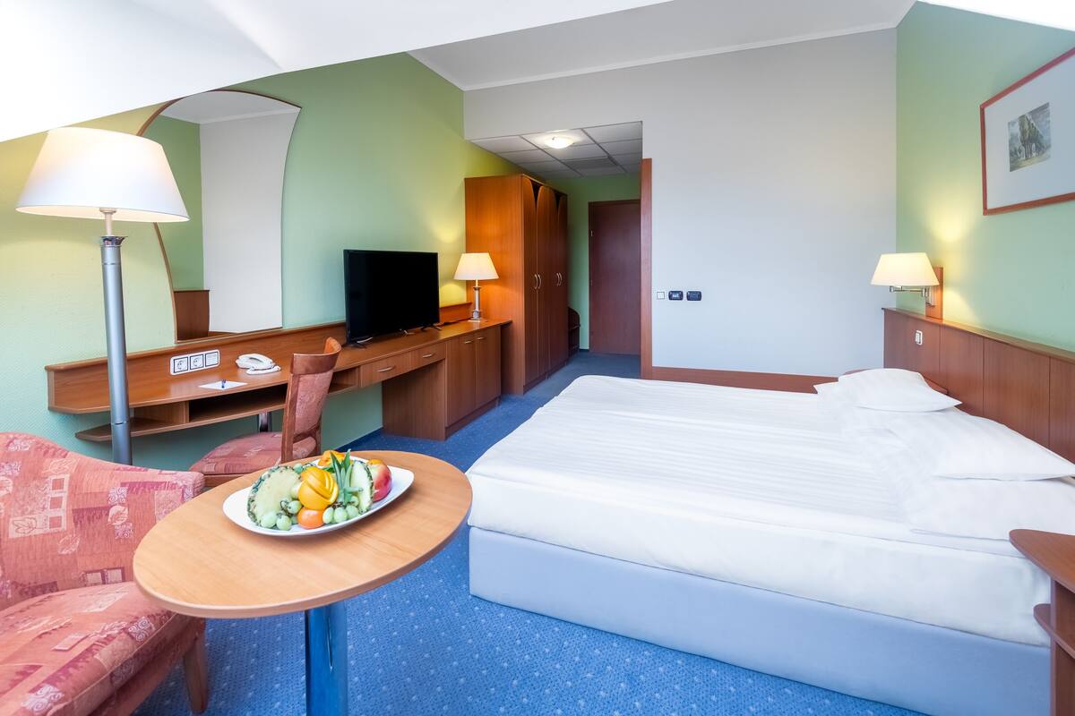 A hotel room with a bed, a desk, a chair, a television, a lamp, and a plate of fruit.